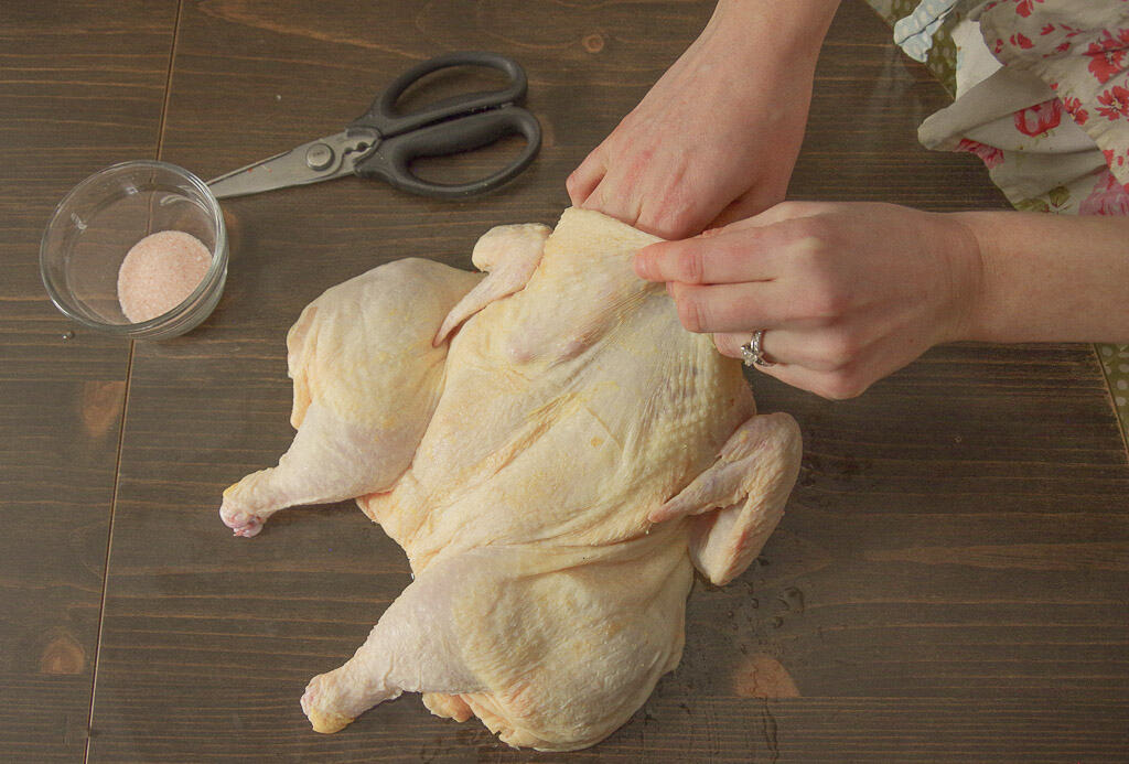 Woman using hand to separate skin from chicken breast meat