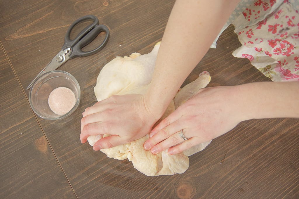 Hands pressing on raw chicken with a bowl of salt and scissors next to it