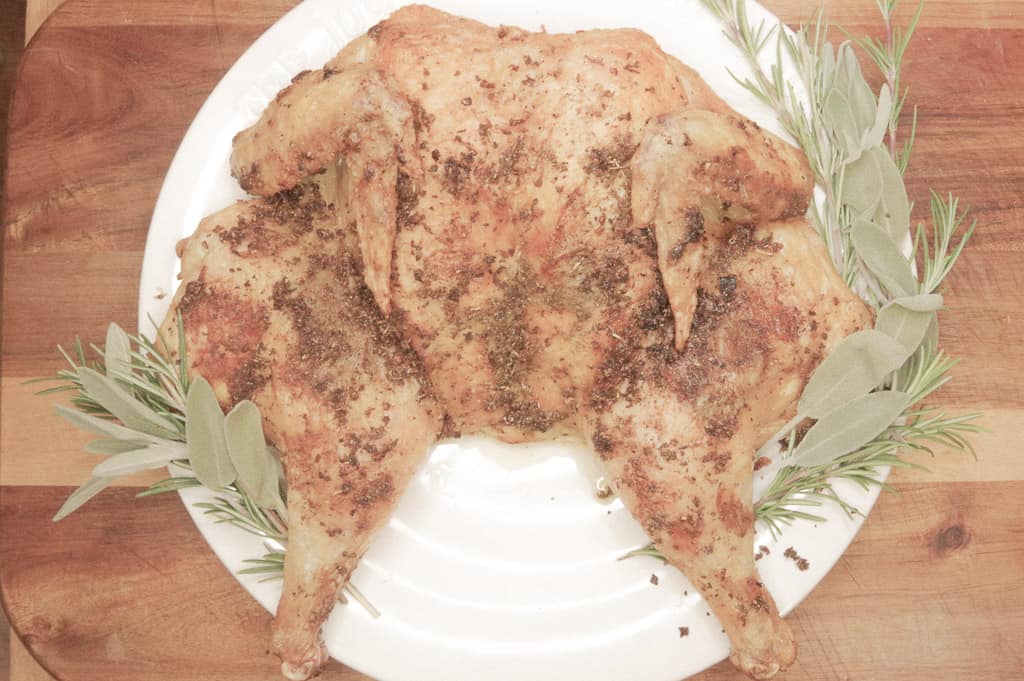 Whole roasted chicken surrounded by herbs 
