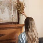 Woman placing dried wheat in a canister on fireplace mantle