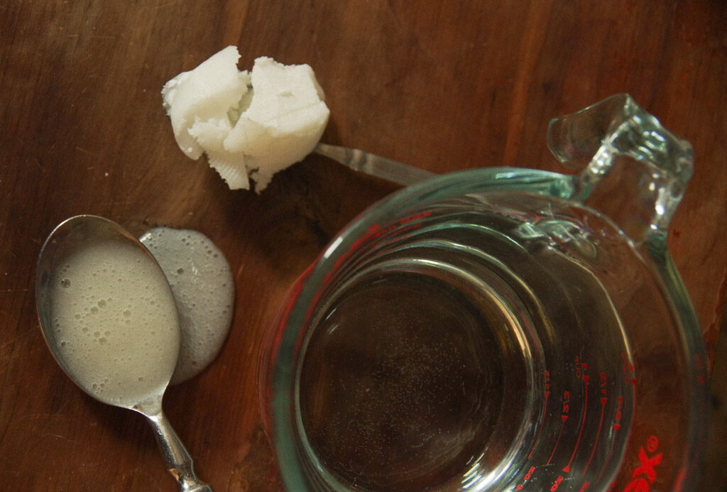 Water in glass measuring cup, spoon of coconut oil, spoon of soap