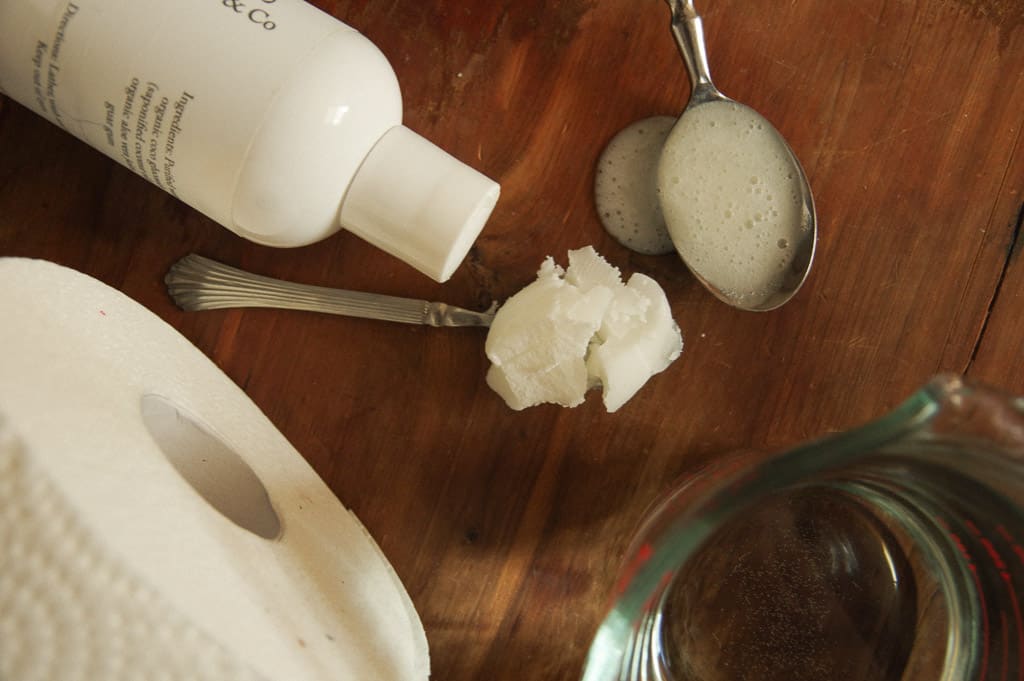 Close-up of soap bottle, paper towel roll, water, coconut oil and soap falling off of a spoon. 