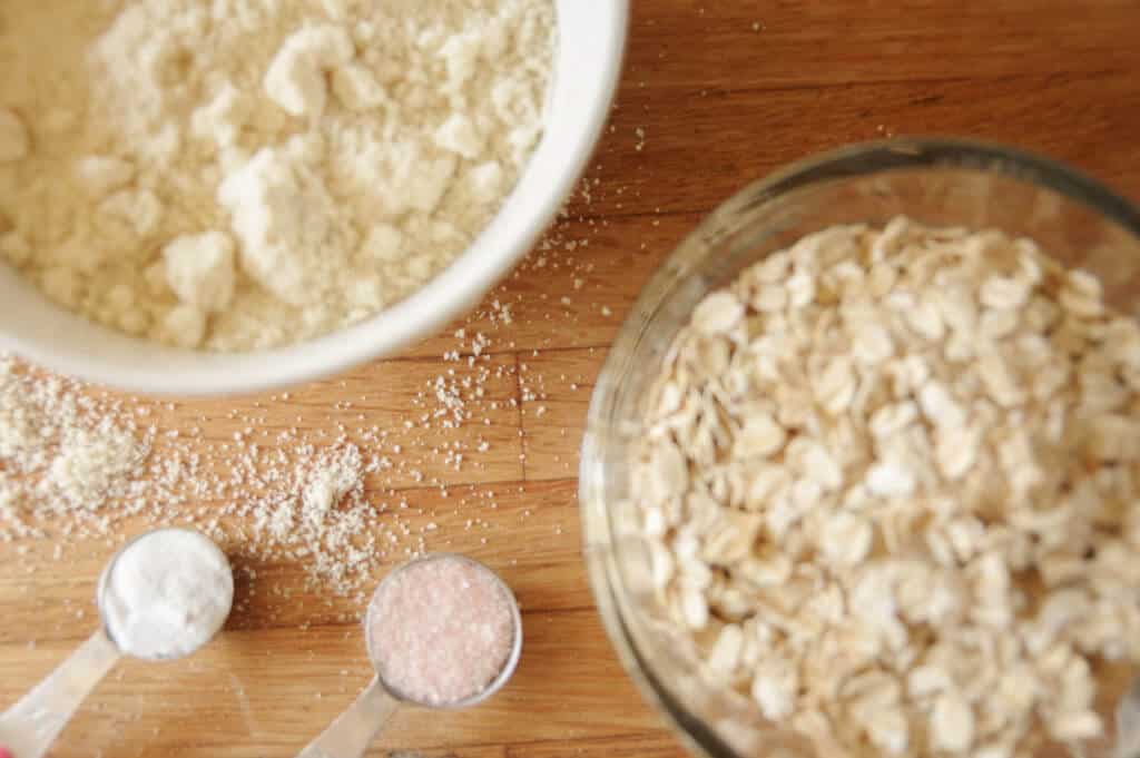 Close up of a bowl of flour, oats and 2 measuring spoons with baking soda and salt on a counter