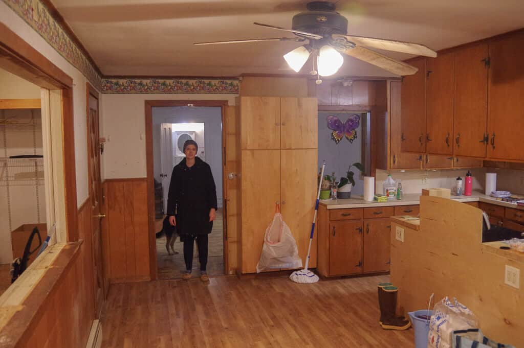 Woman standing in kitchen doorway wearing a black coat. 