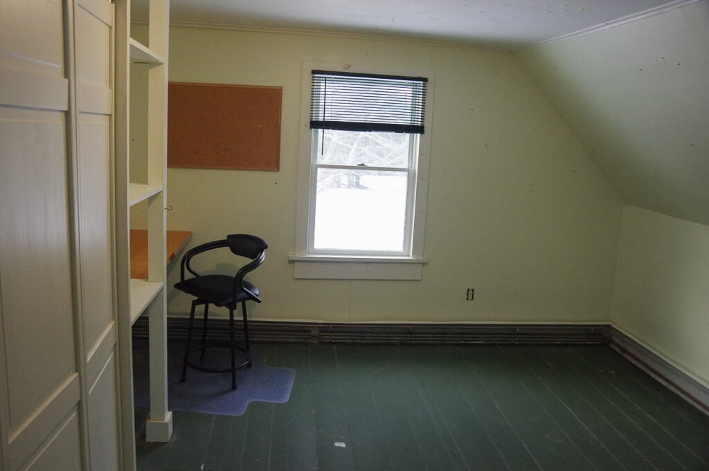 Room with grey floor and light green walls. Window, desk and chair
