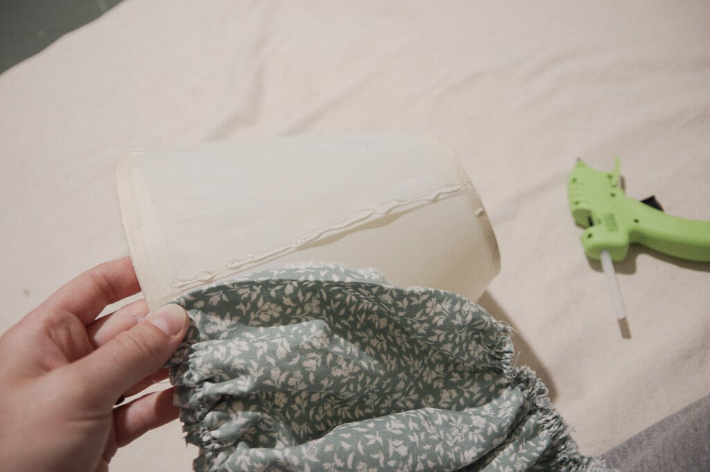 Hand holding fabric on lampshade with hot glue on it