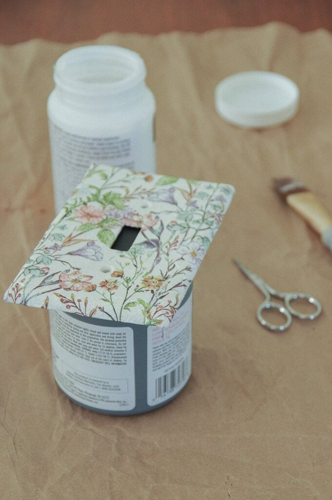 Light switch cover placed on top of can next to scissors and paintbrush