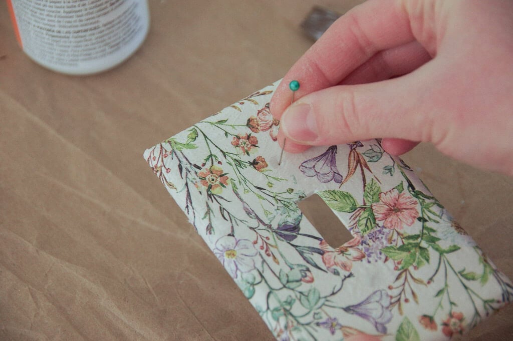 Hand using sewing pin to poke a light switch plate cover