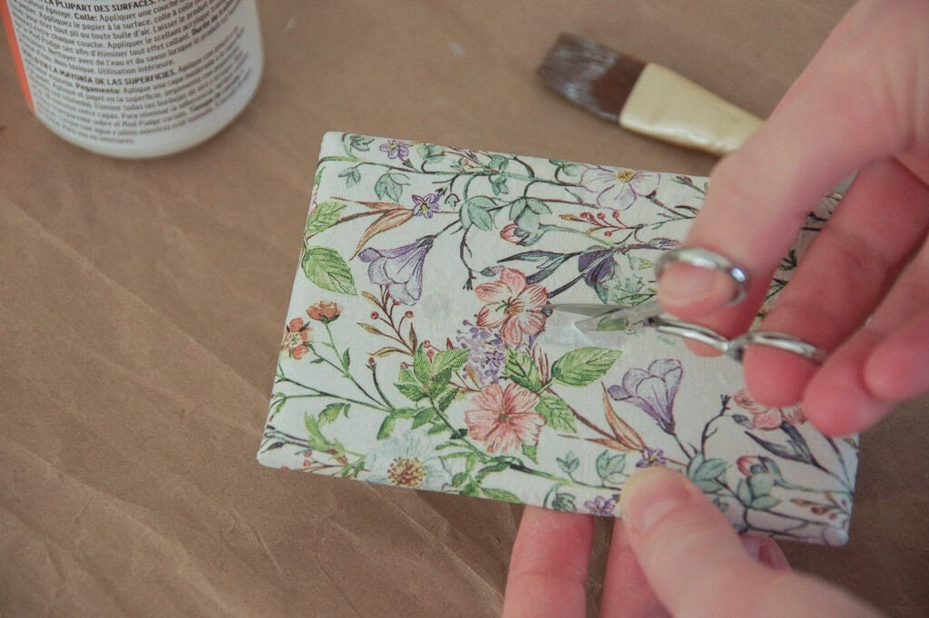 Hand using scissors to cut a small slit in the hole of a light switch plate covered with paper 