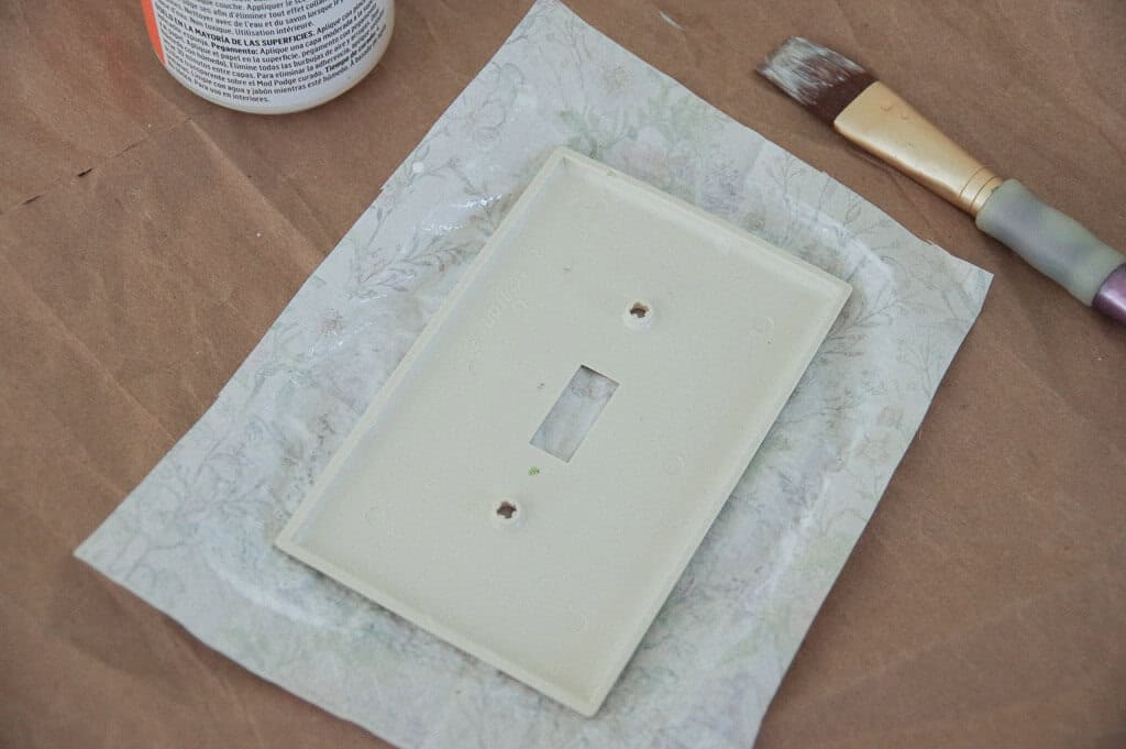 Light switch plate upside down on paper next to paint brush