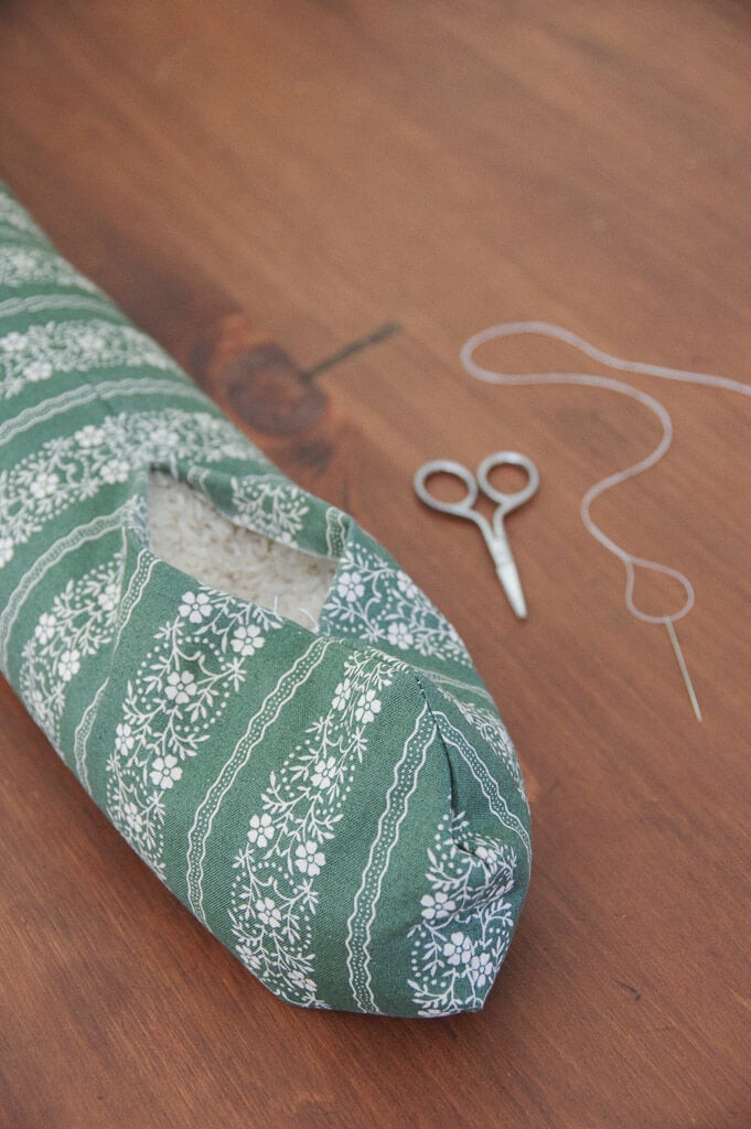 Fabric tube filled with rice with scissors and thread next to it