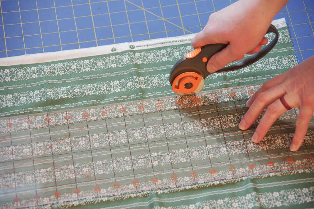 Hands using rotary cutter to cut fabric