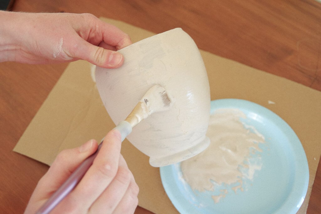 Hands holding pottery and using a paintbrush to paint on it