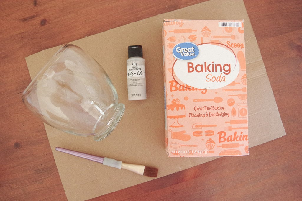 Glass vase on table next to paintbrush, craft paint and baking soda