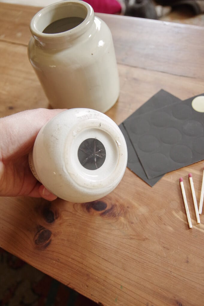 Hand holding white jar with black dot on the bottom