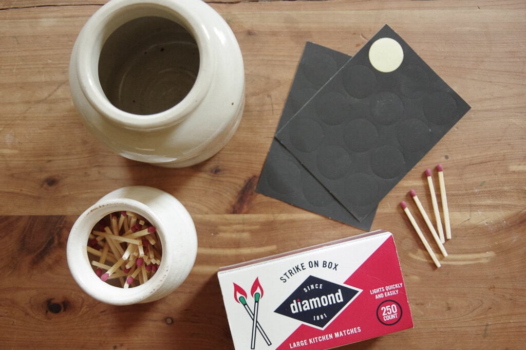 Jars, black paper, matches, match stick box on wooden surface