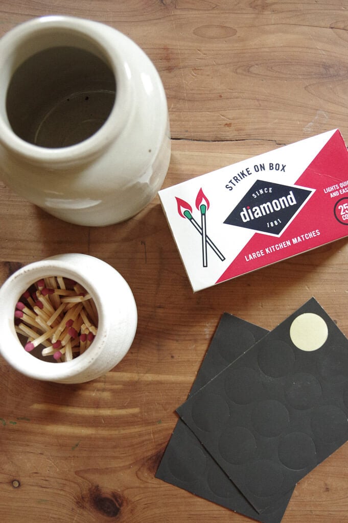 Ceramic jars, black paper and box of matches on wooden table
